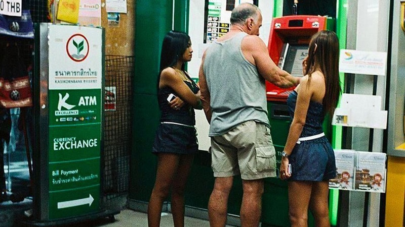 A foreigner taking money out of ATM with 2 Thai girls